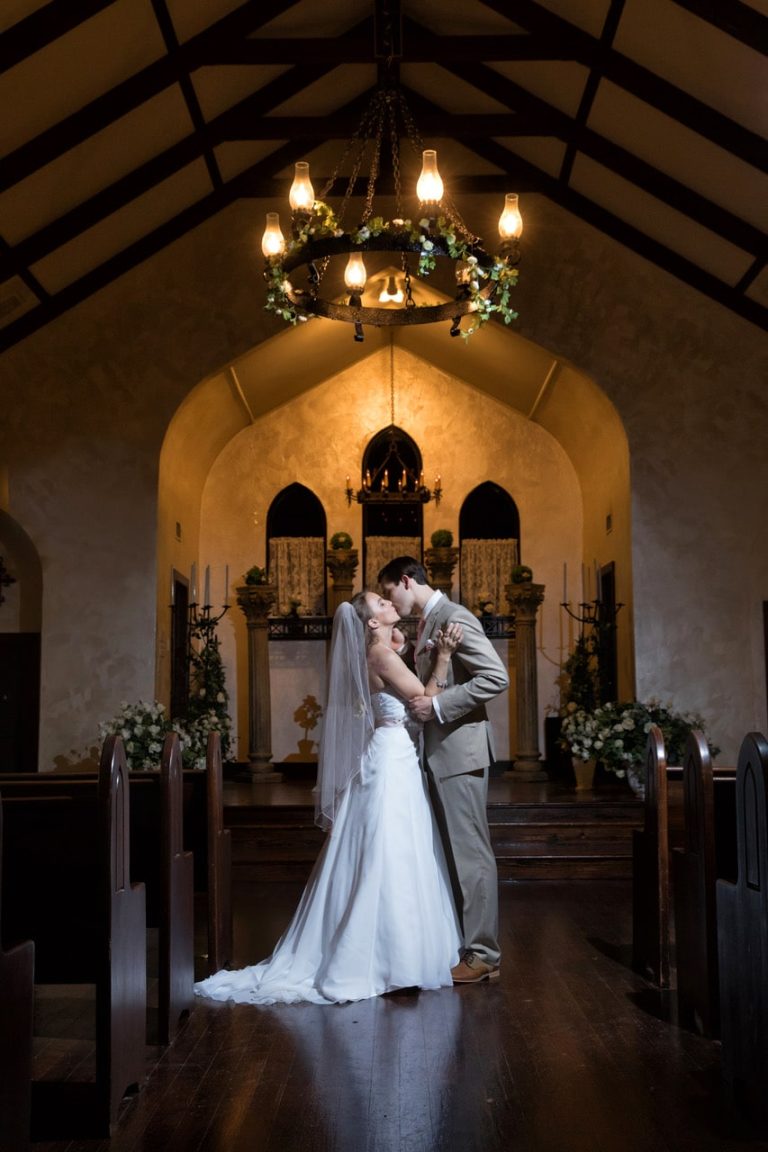 Bride and groom kiss in historic wedding chapel.